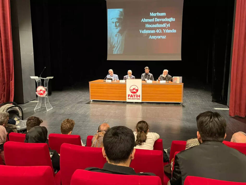 Ahmed Davudoğlu için yapılan anma programı fotoğrafı. Konferans salonundaki insanlar konuşmacıları dinliyor.